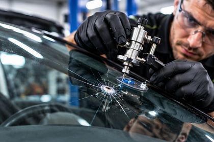 Technician repairing a stone chip in a car windscreen with a resin injector
